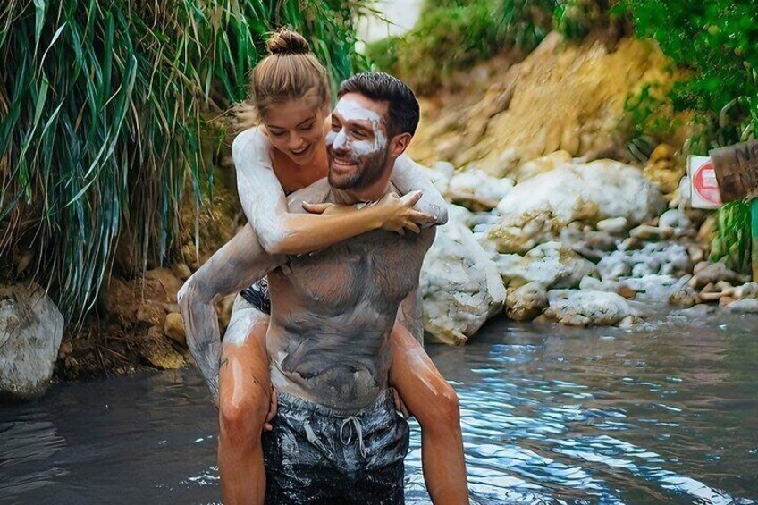 A person carrying another on their shoulders in a natural water setting with rocks and vegetation. 1