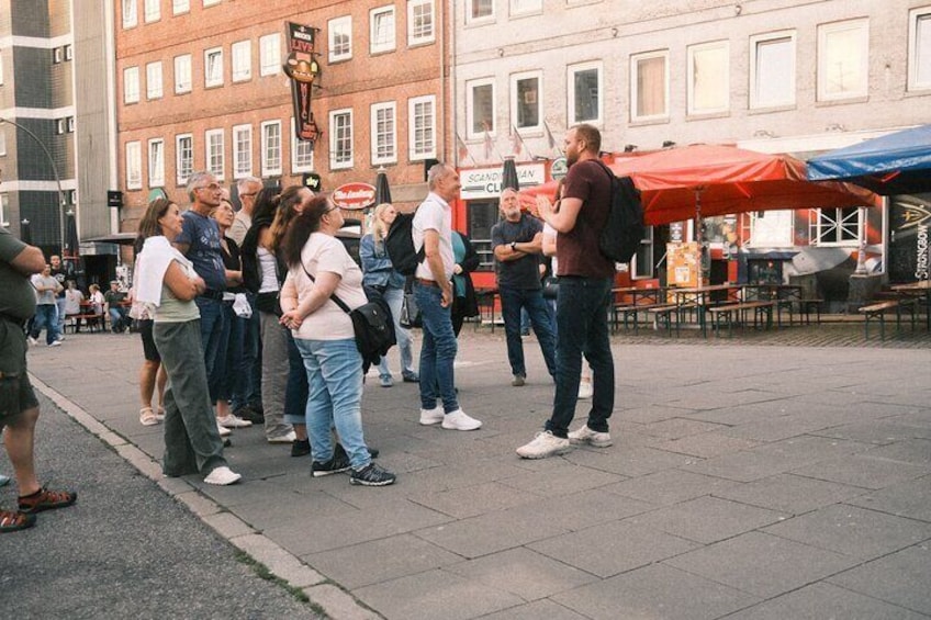 Een groep mensen staat op een straat, met gebouwen en terrasjes op de achtergrond. 4