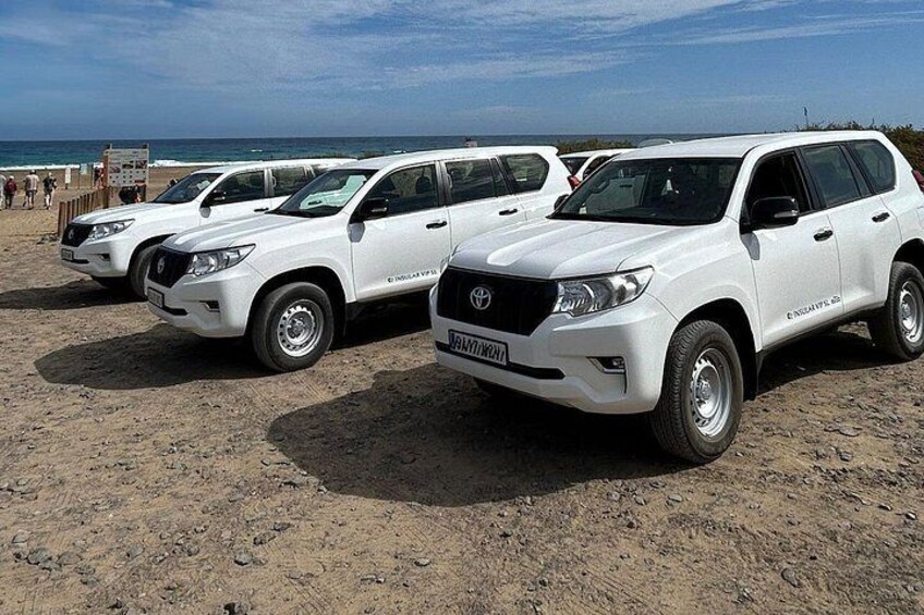 Three white SUVs parked on a sandy beach with the ocean in the background. 2