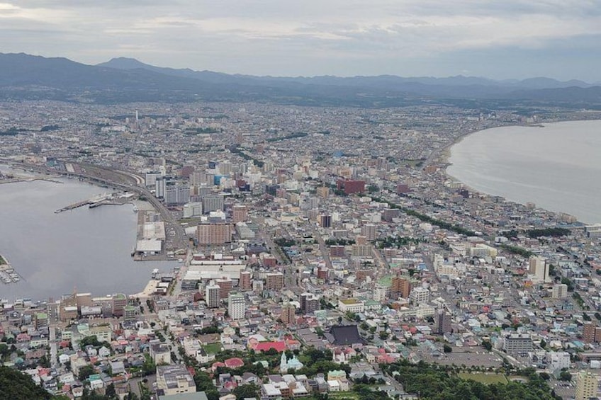 A coastal cityscape with a dense urban area, a large body of water, and distant mountains. 5