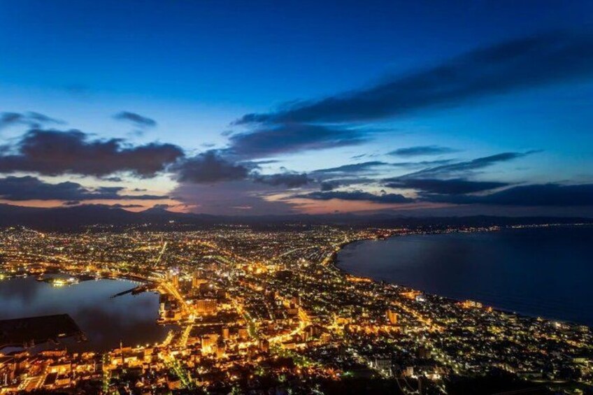 Une vue d’une ville au crépuscule, avec une côte, des rues illuminées et une vaste étendue d’eau. 2