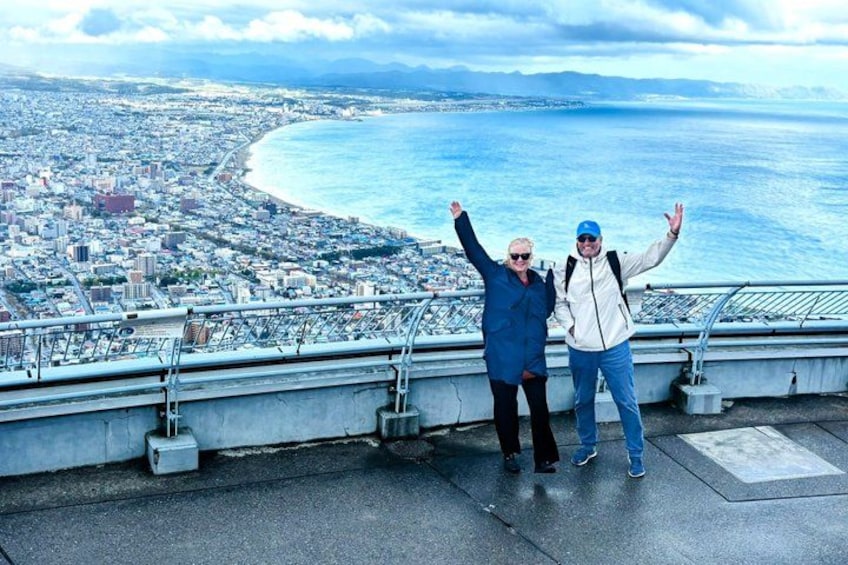 Deux personnes se tiennent sur une plateforme d’observation, avec une vue sur le paysage urbain côtier en arrière-plan. 1