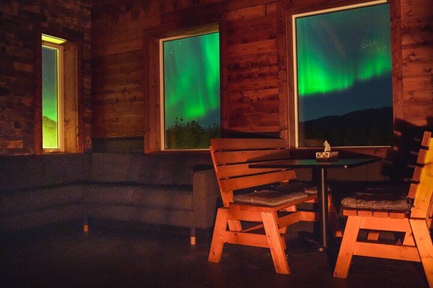 A wooden cabin interior with a table and chairs, windows with a view of the aurora borealis. 3