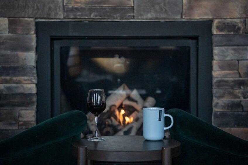 A fireplace with a glass door, a wine glass, and a white mug on a small table. 5