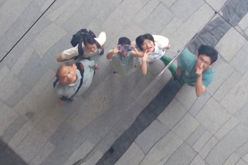 A group of people standing on a tiled pavement, some holding a smartphone. 4