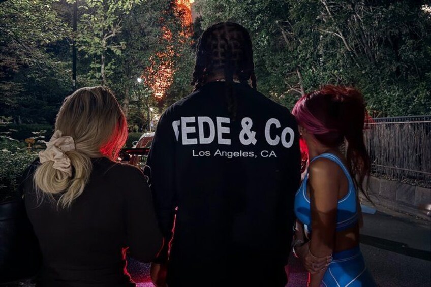 Three people walking on a bridge with trees and lights in the background. 3