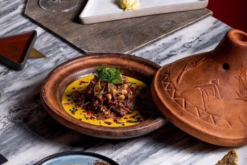 A clay dish with a stew, a ceramic plate with a yellow sauce, and a terracotta pot on a marble table. 1