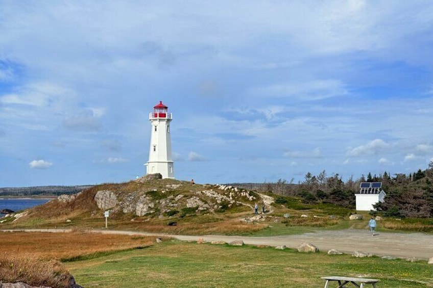 Ett vitt fyrtorn med en röd topp, beläget på en grönskande kulle vid havet. 1