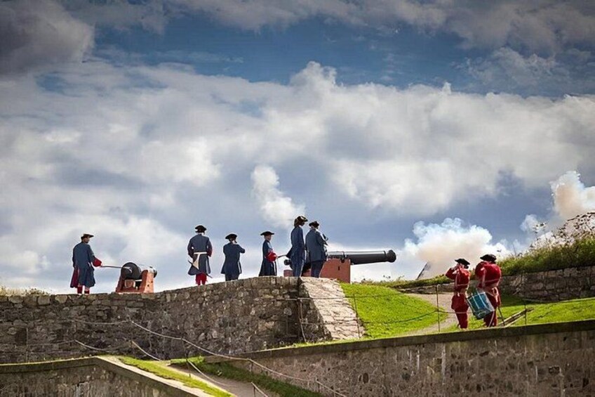 A historical reenactment with people in period costumes, a cannon, and a stone fortification. 1