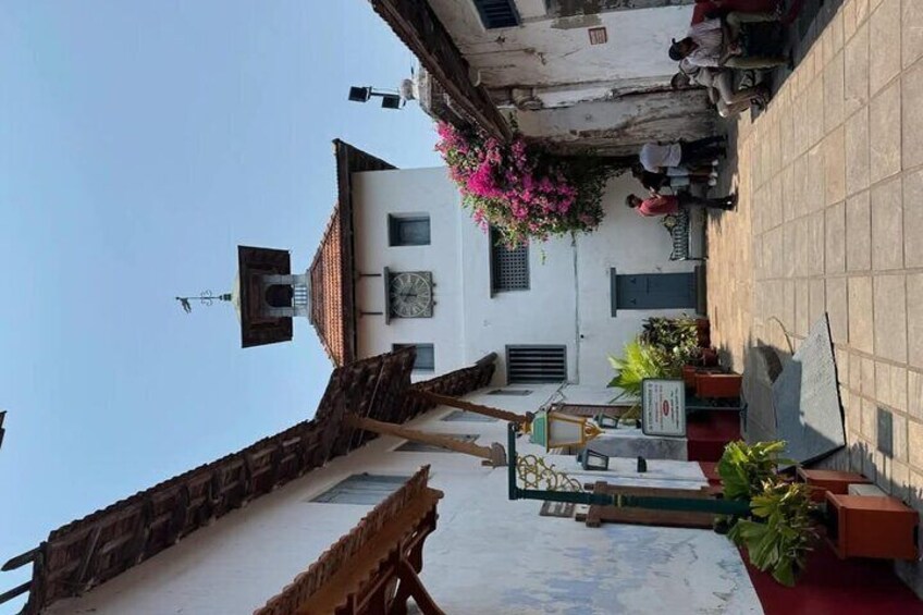 Una stretta via fiancheggiata da edifici, con una torre dell'orologio e vasi di piante. 2