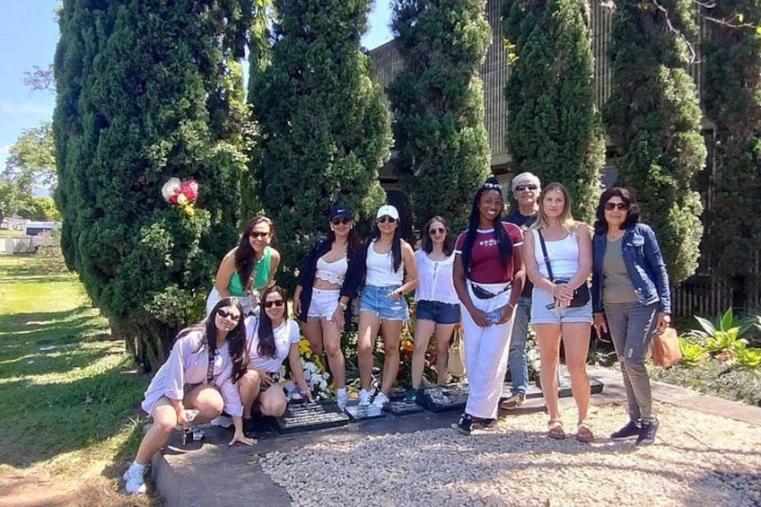 A group of people posing in a garden with tall trees and a gravel path. 5