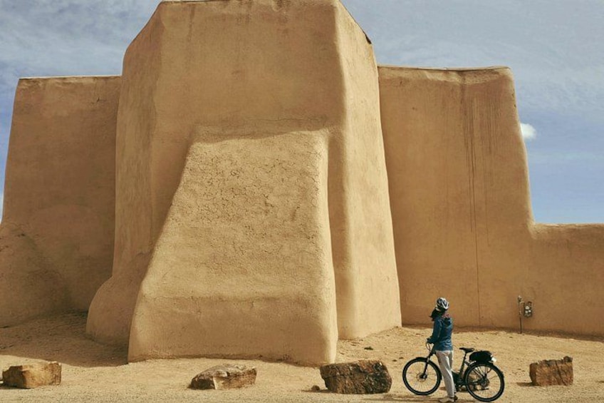 A person on a bicycle in front of a large, sandy structure with a steep incline. 1