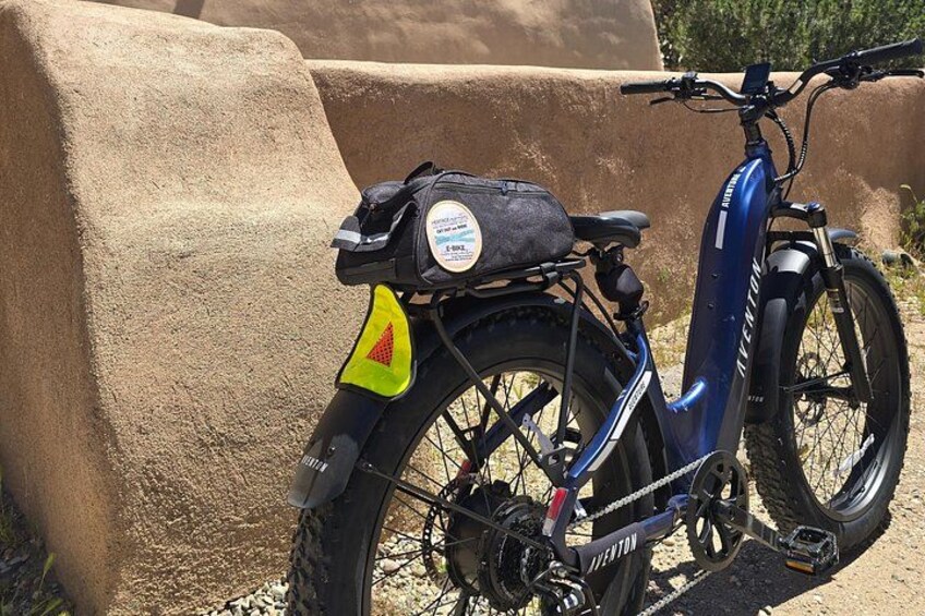 Una bicicleta eléctrica azul con un portaequipajes trasero y un reflector amarillo en la rueda trasera. 4