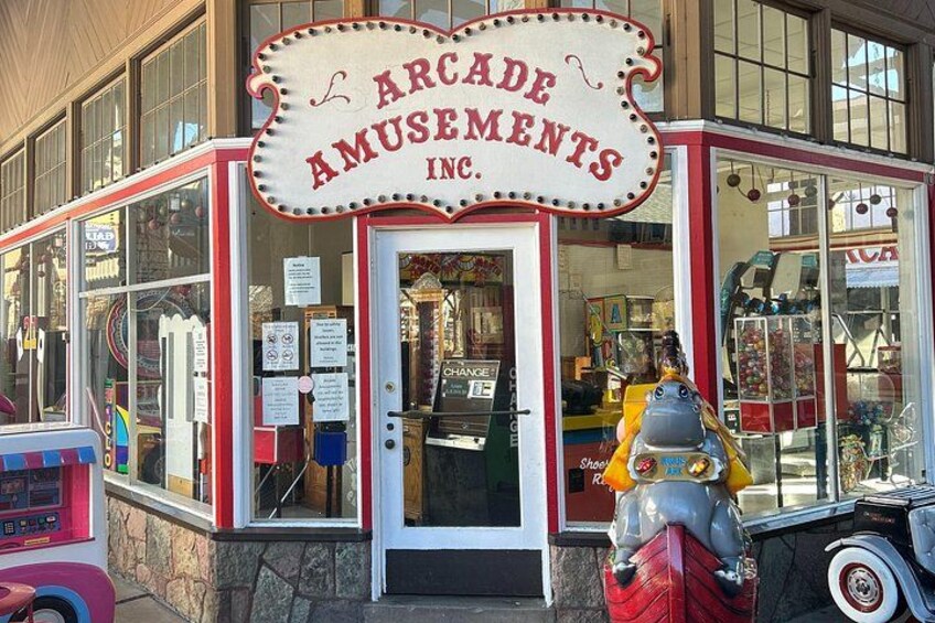 A storefront with a sign reading 'Arcade Amusements Inc.' and a vintage car parked in front. 3