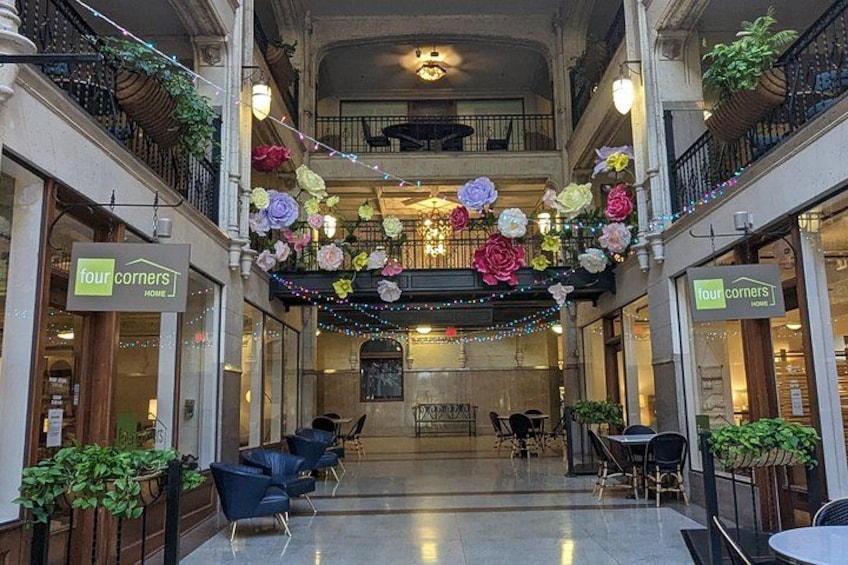 En atriumliknande innergård i ett köpcentrum med en central blomsterarrangemang, sittplatser och butikslokaler. 3