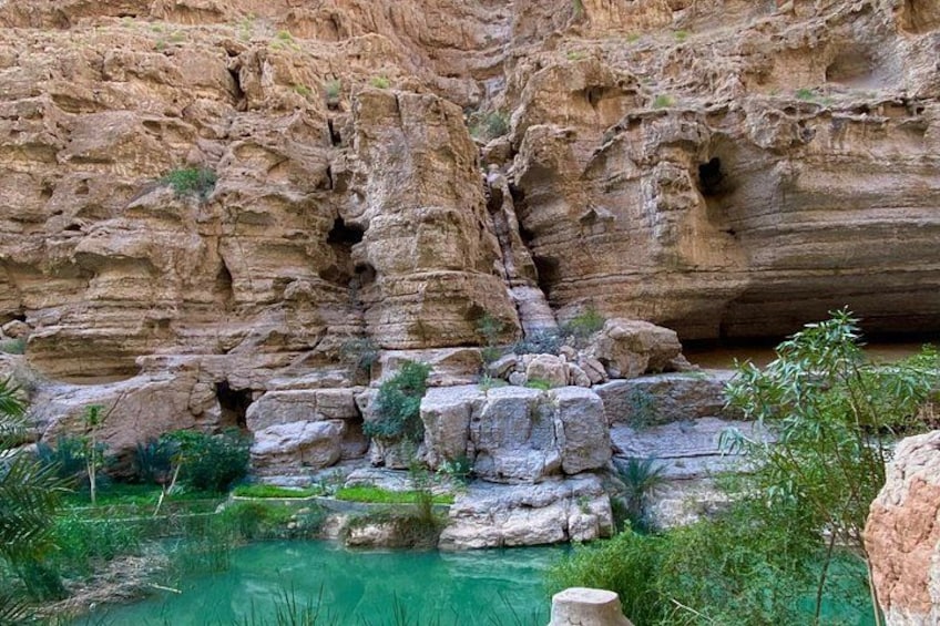 A canyon with layered rock formations, a clear turquoise pool, and some greenery. 2