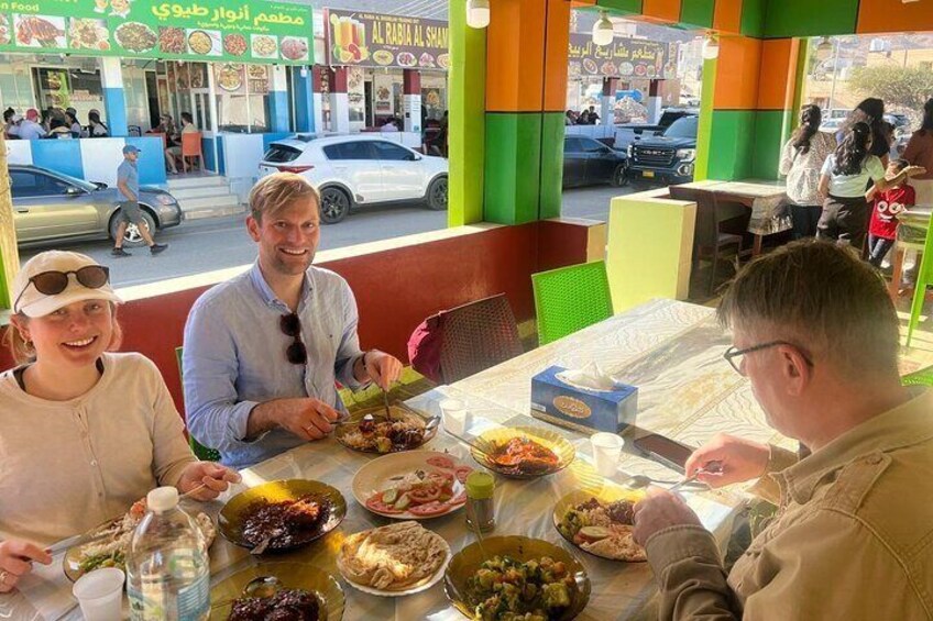 Eine Gruppe von Personen speist in einem Restaurant mit farbenfroher Einrichtung und Blick auf die Straße. 2