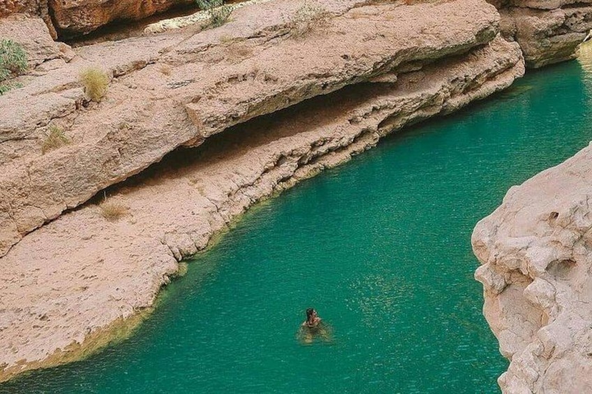 Eine Person schwimmt in einem türkisfarbenen Fluss, umgeben von felsigem Gelände. 2