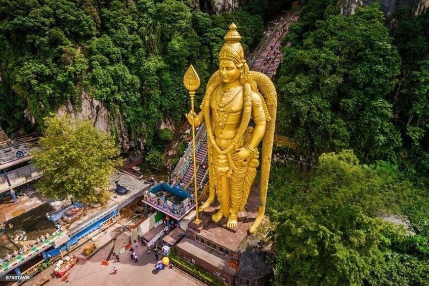 A large golden statue of a deity with a staff, surrounded by lush greenery and a temple structure. 2