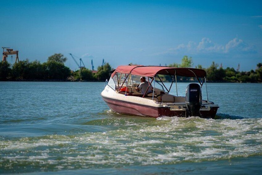 A small motorboat with a canopy, moving on calm water with a clear sky and distant shoreline. 5