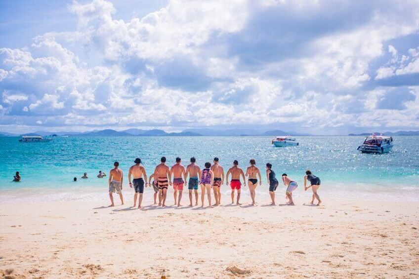 Una playa con gente de pie y caminando por la orilla, barcos en el agua y un cielo despejado. 1