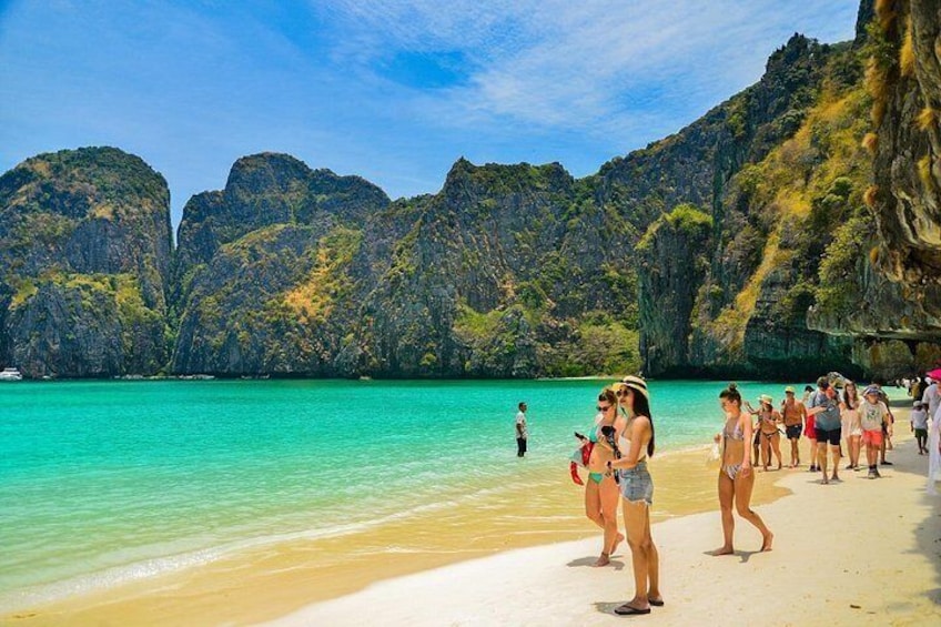 Una playa con agua turquesa cristalina, gente caminando y acantilados rocosos al fondo. 1
