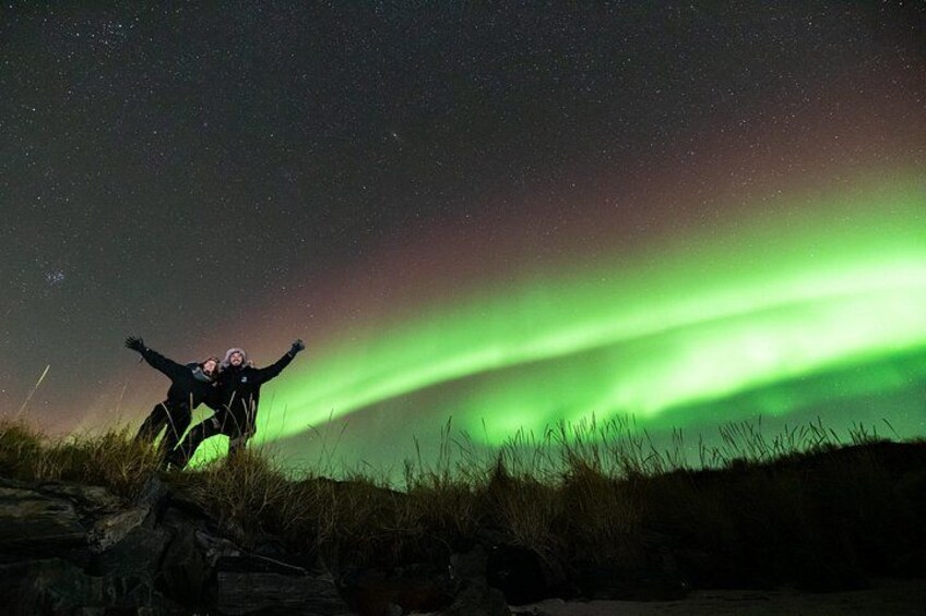 A person standing on a rocky outcrop under a night sky with the aurora borealis. 4