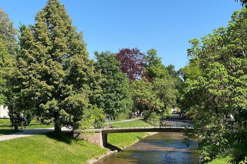 A park with a bridge over a stream, surrounded by trees and a clear sky. 2