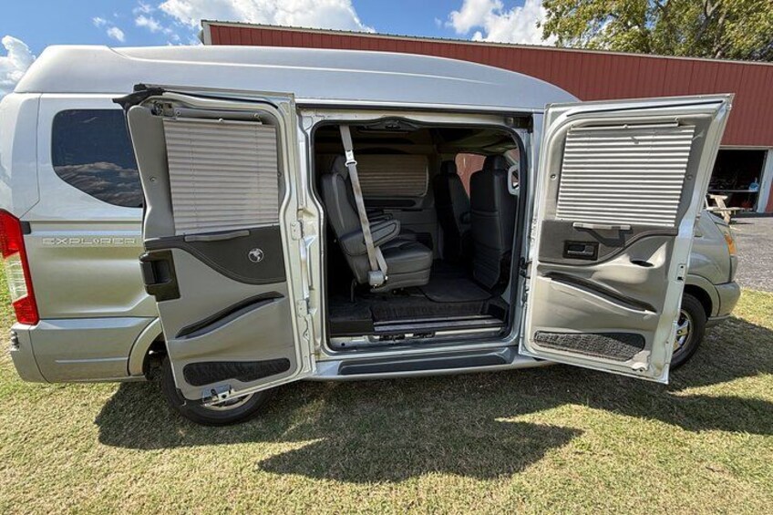 A silver van with its rear doors open, parked on grass with a building in the background. 3