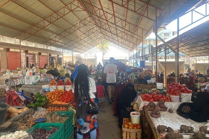 Un mercado techado concurrido, con varios puestos que ofrecen frutas, verduras y otros productos. 2