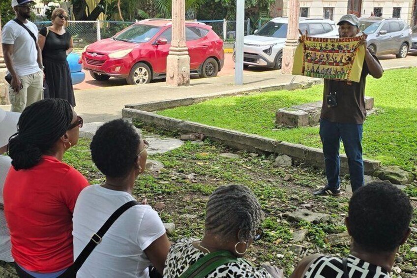 A group of people gathered outdoors, some holding signs, with a red car and a building in the background. 2
