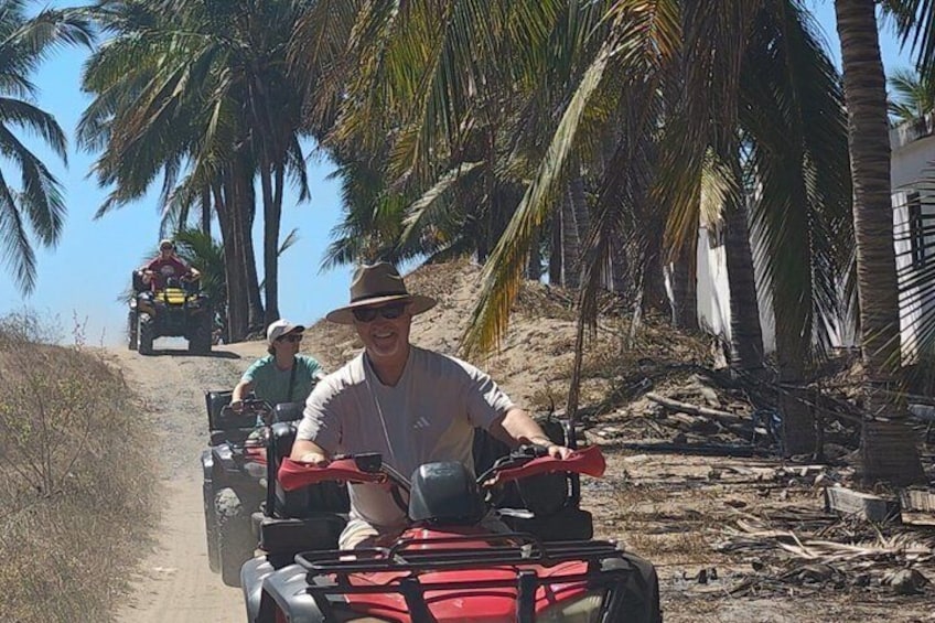 A person riding an ATV on a dirt path with palm trees in the background. 2
