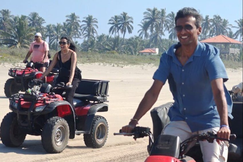 People riding ATVs on a sandy beach with palm trees in the background. 5