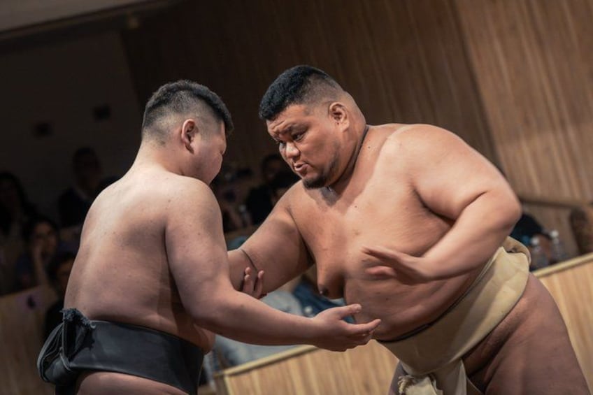 Two sumo wrestlers in a match, with an audience in the background. 1