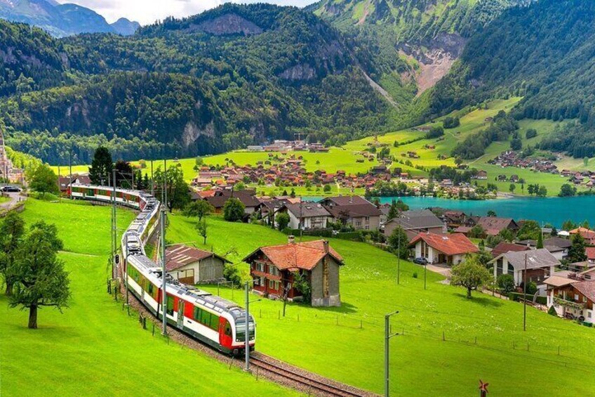 A train traveling through a lush green valley with houses and a lake. 1