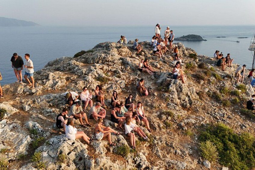 A rocky coastal area with people sitting and standing on the cliffs, overlooking the sea. 2