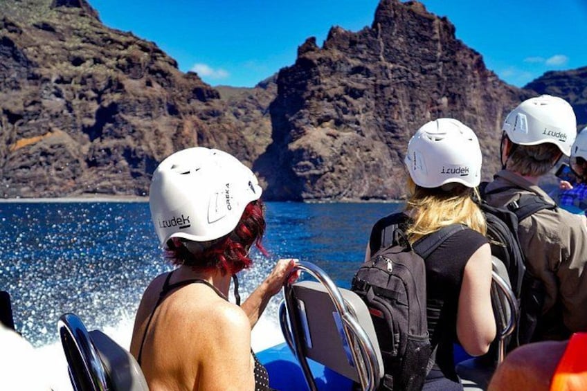 People on a boat wearing helmets and life jackets, with rocky cliffs and water in the background. 3
