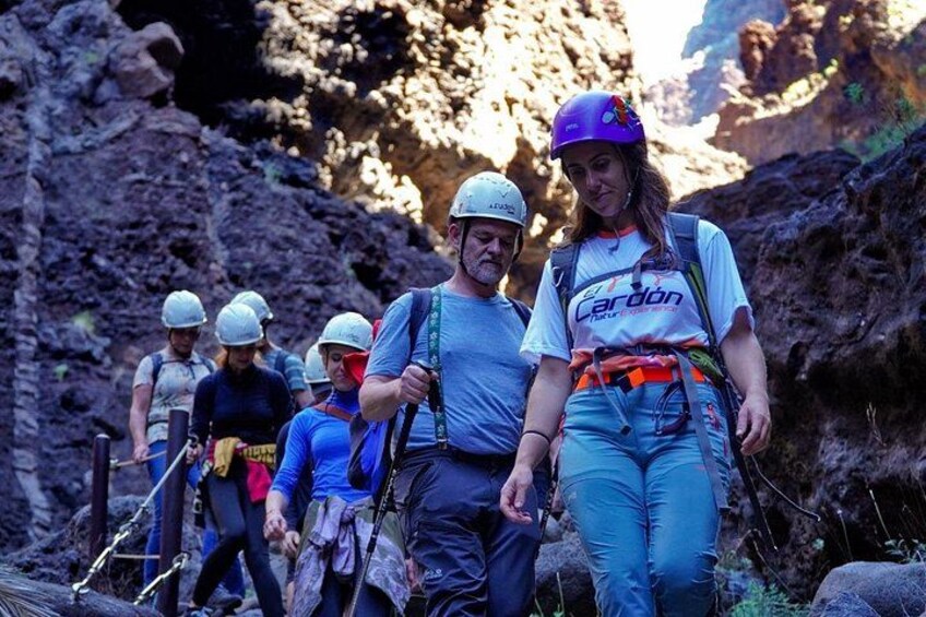 A group of people hiking in a rocky canyon with helmets and backpacks. 1