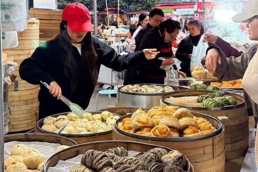 Ein Straßenverkäufer bereitet Essen an einem Marktstand zu, wo verschiedene Speisen ausliegen. 2
