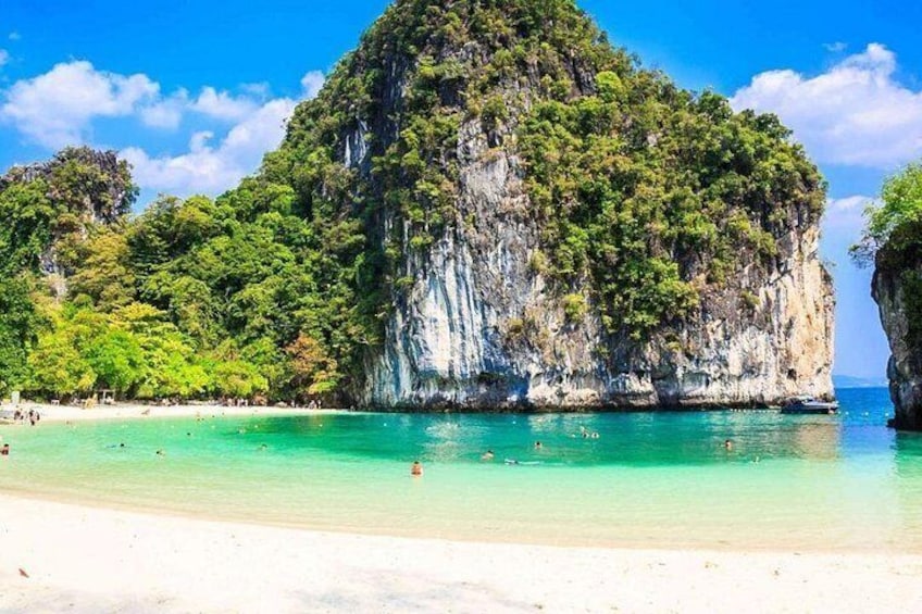 A beach with clear turquoise water, a large limestone cliff, and lush greenery. 2