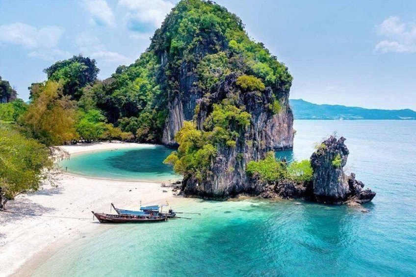 A beach with clear turquoise waters, a boat, and a large rock formation. 4