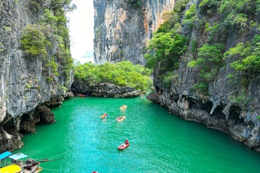 A group of people kayaking in a narrow, green waterway surrounded by rocky cliffs. 1