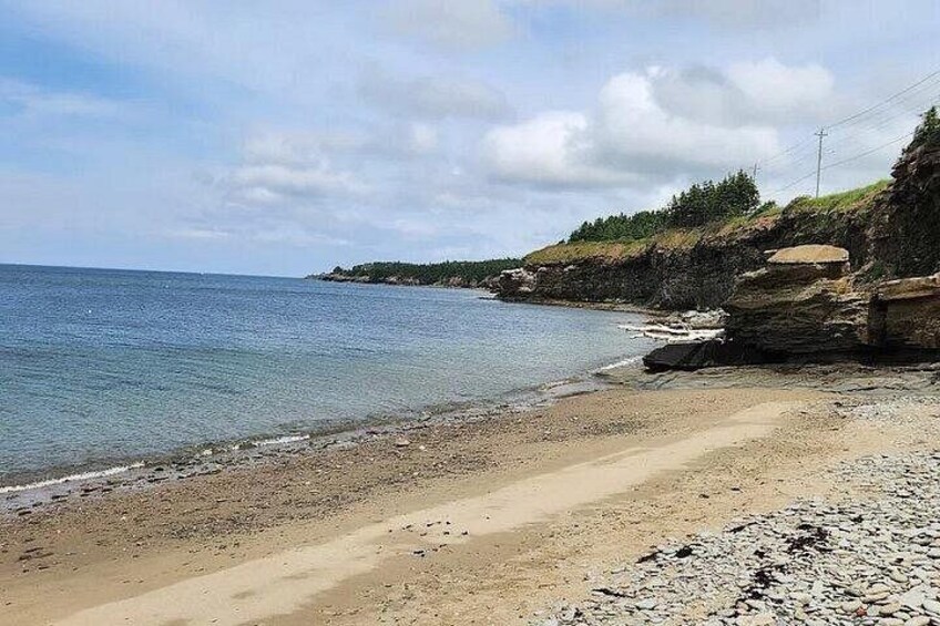A coastal beach with a rocky shoreline, calm sea, and a distant forested hill. 2