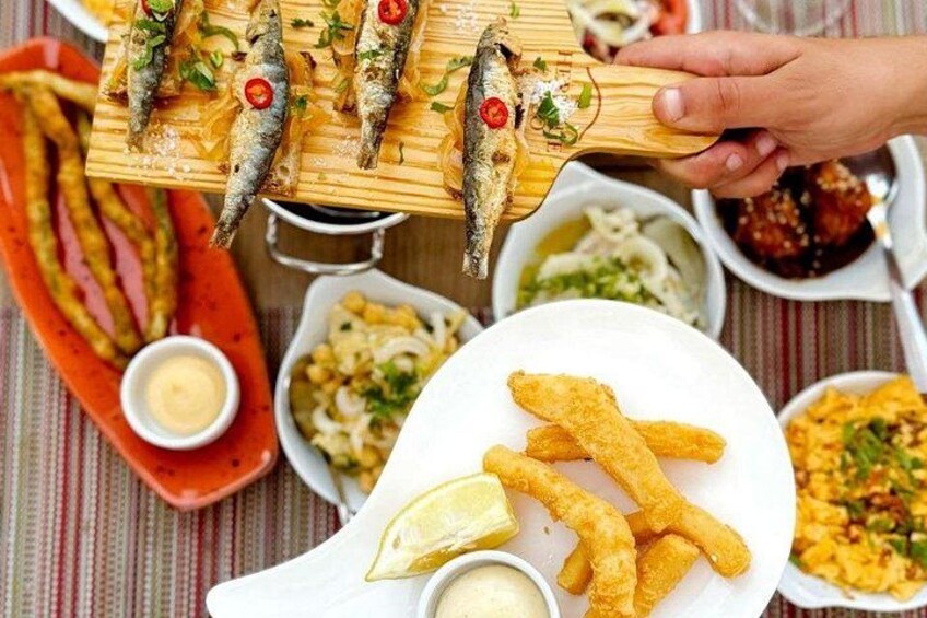 Una tabla de madera con pescado a la parrilla, un plato de frituras y varios acompañamientos. 2