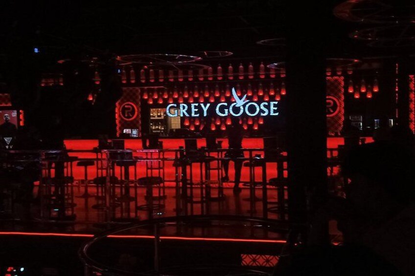 A bar with a neon sign reading 'GREY GOOSE' and red lighting. 5