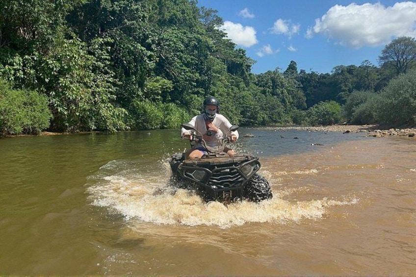 A person riding an ATV through a river surrounded by dense greenery. 4