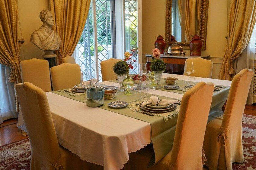Un comedor con una mesa dispuesta para cuatro personas, sillas alrededor, un busto en la pared y una ventana con cortinas. 3