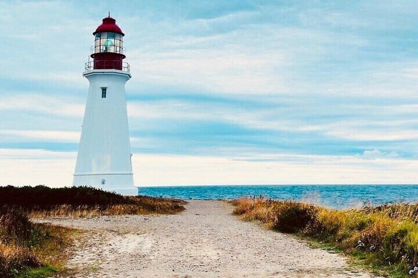 A white lighthouse with a red top, a gravel path leading to it, and the ocean in the background. 5