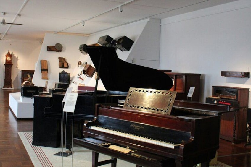 A grand piano in a museum setting with various antique items in the background. 5