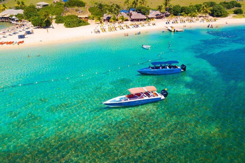 A tropical beach with clear turquoise waters, several boats, and a sandy shore with beach umbrellas and people. 4